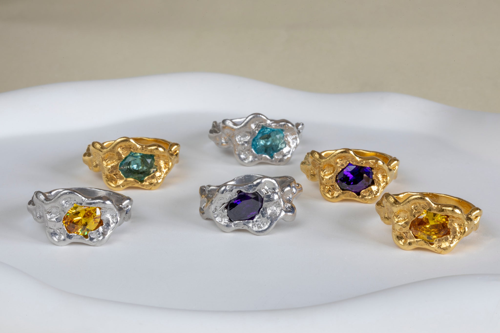 Set of six gemstone rings in gold and silver on a white surface